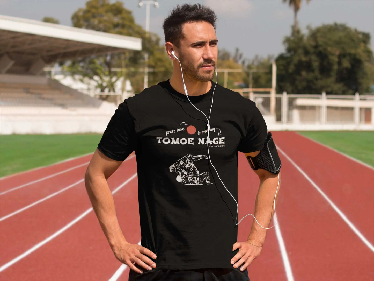 Athletic man on a running track wearing a black Judo T-Shirt with 'Press Here to Meet My Tomoe Nage' design, paired with workout gear.
