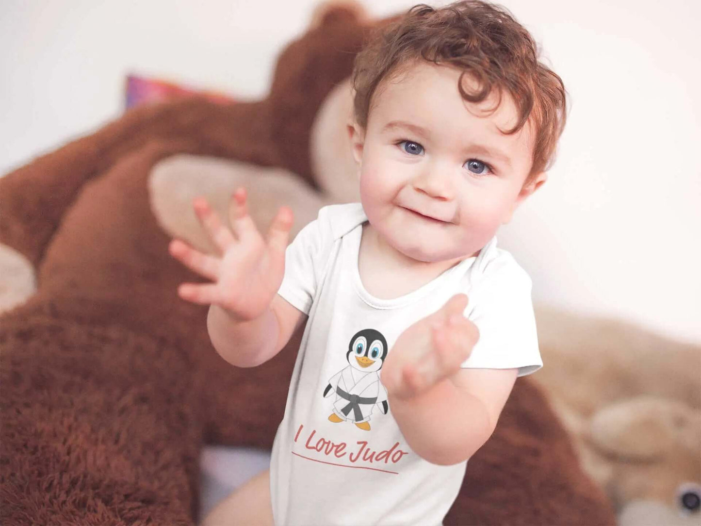Adorable baby wearing a white Judo Baby Bodysuit featuring a cute penguin design and 'I Love Judo' text. Perfect for baby and toddler wear.