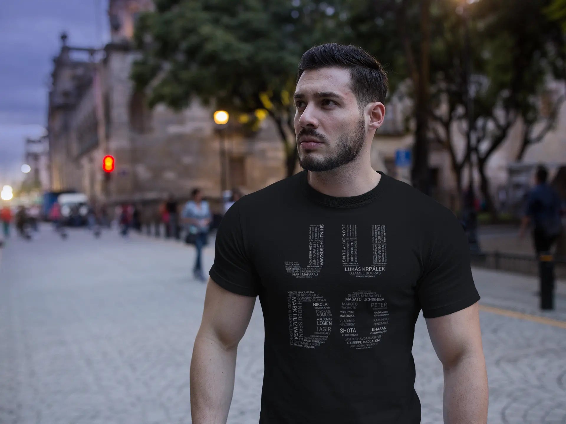 Model wearing the Judo Olympic Winners T-Shirt in a casual outdoor setting, showcasing the bold design of Olympic judo legends' names.
