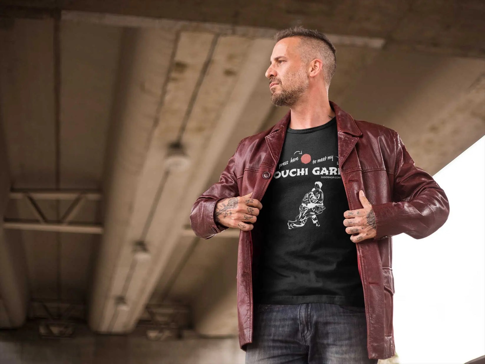 Man wearing a black 'Ouchi Gari Press Here' Judo T-Shirt under a red leather jacket, showcasing casual and sporty style.
