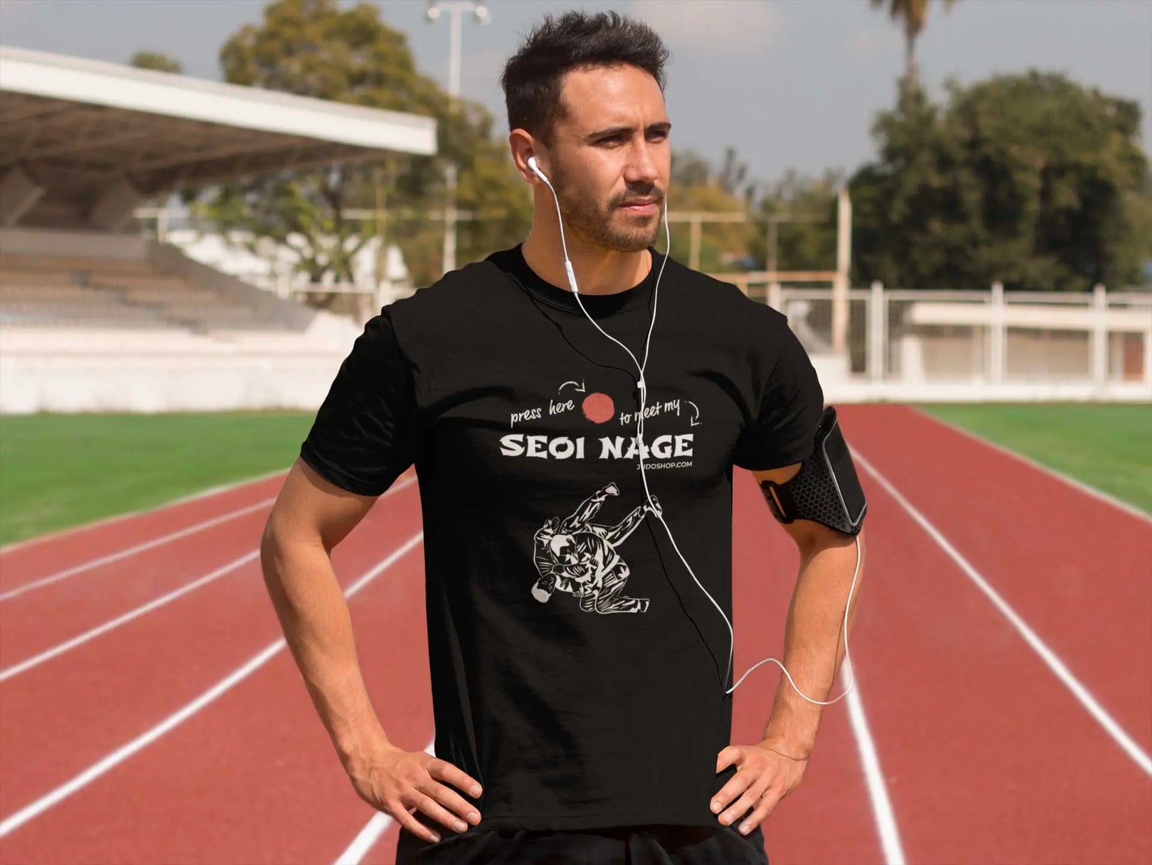 Athletic man on a running track wearing a black Seoi Nage Judo T-Shirt, paired with earphones and an armband.