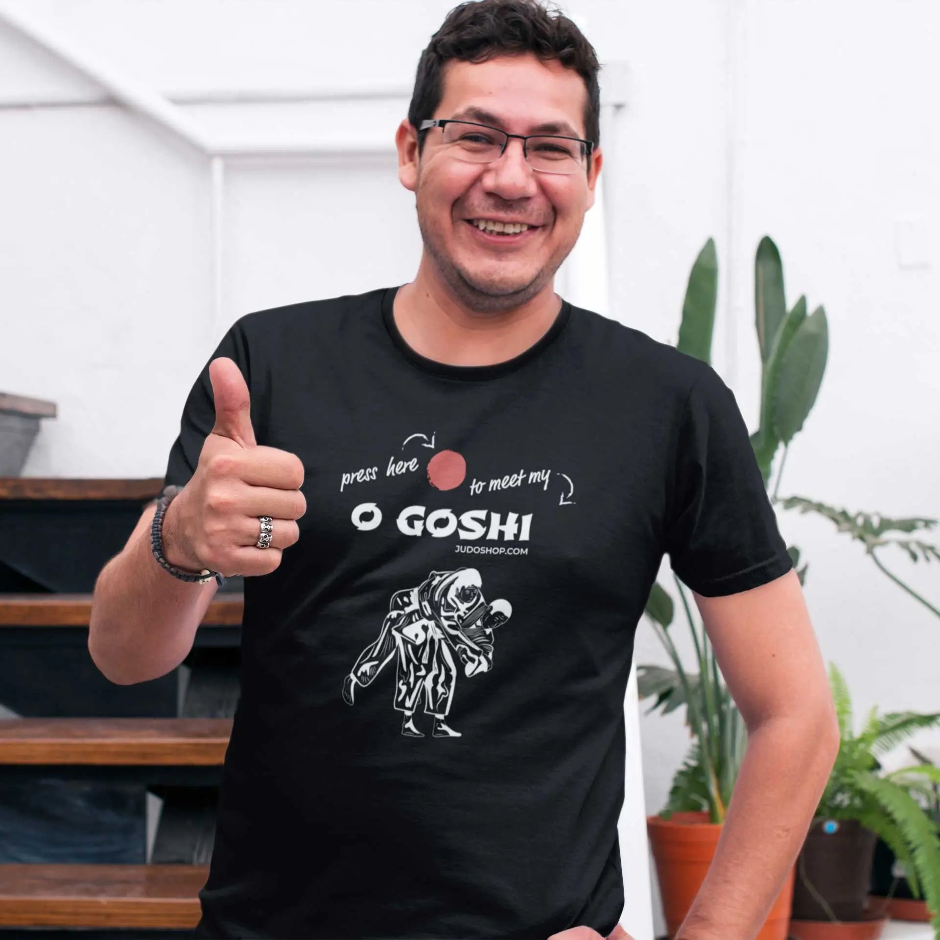 Smiling man giving a thumbs-up while wearing a black Judo T-Shirt with 'Press Here to Meet My O Goshi' design, ideal for casual wear.