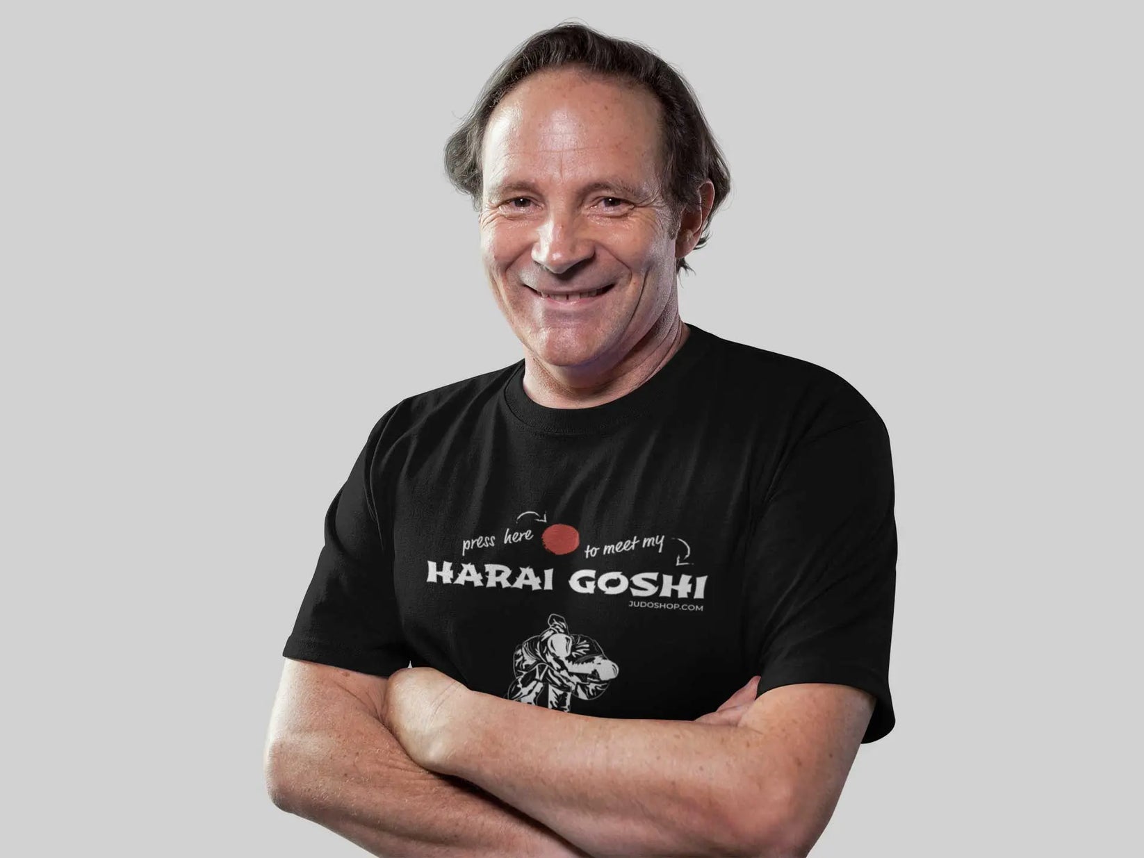 Man smiling in a black 'Harai Goshi Press Here' Judo T-Shirt, styled with arms crossed for a friendly and approachable look.