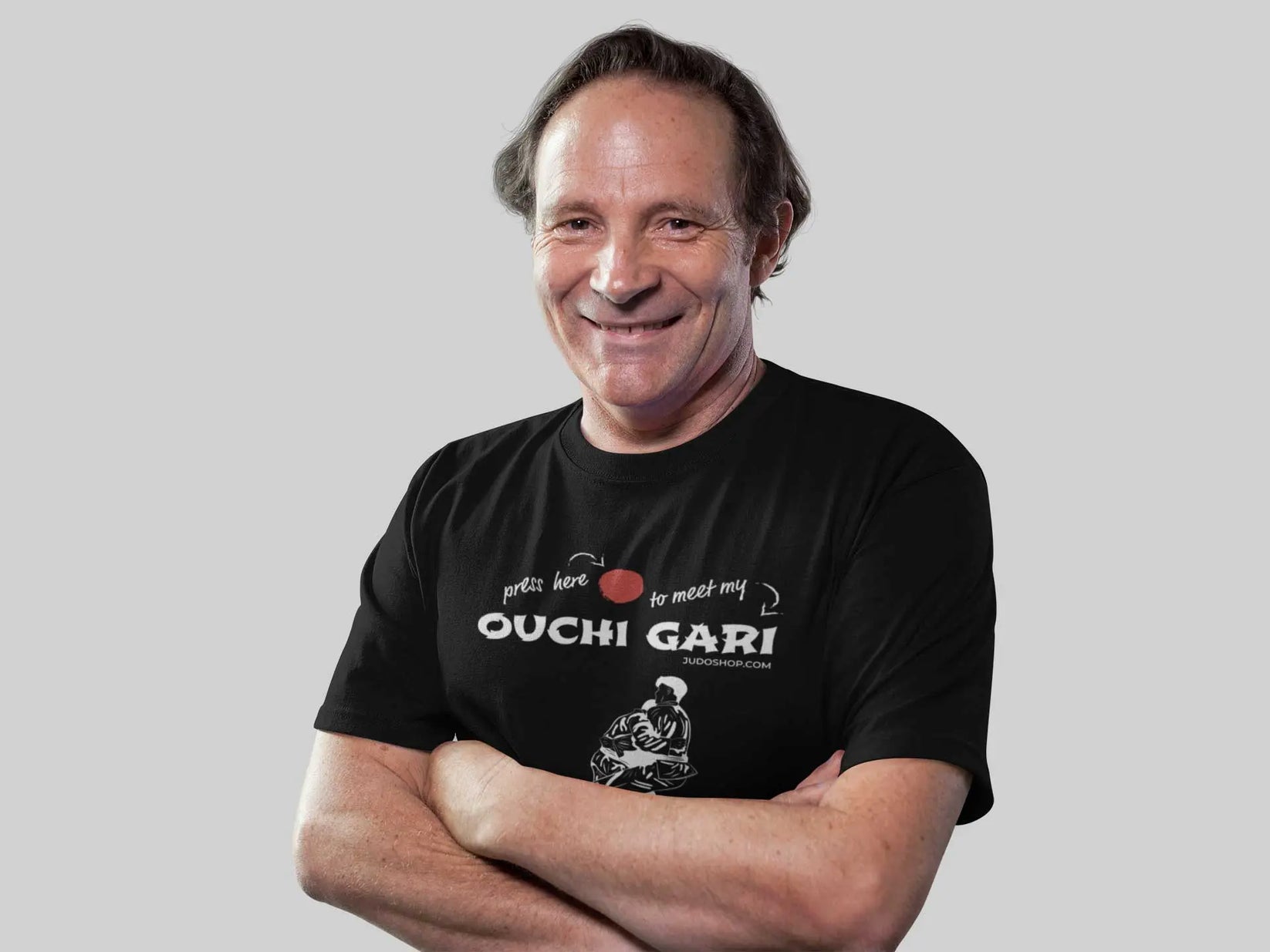 Man smiling confidently in a black 'Ouchi Gari Press Here' Judo T-Shirt, perfect for casual and martial arts enthusiasts.