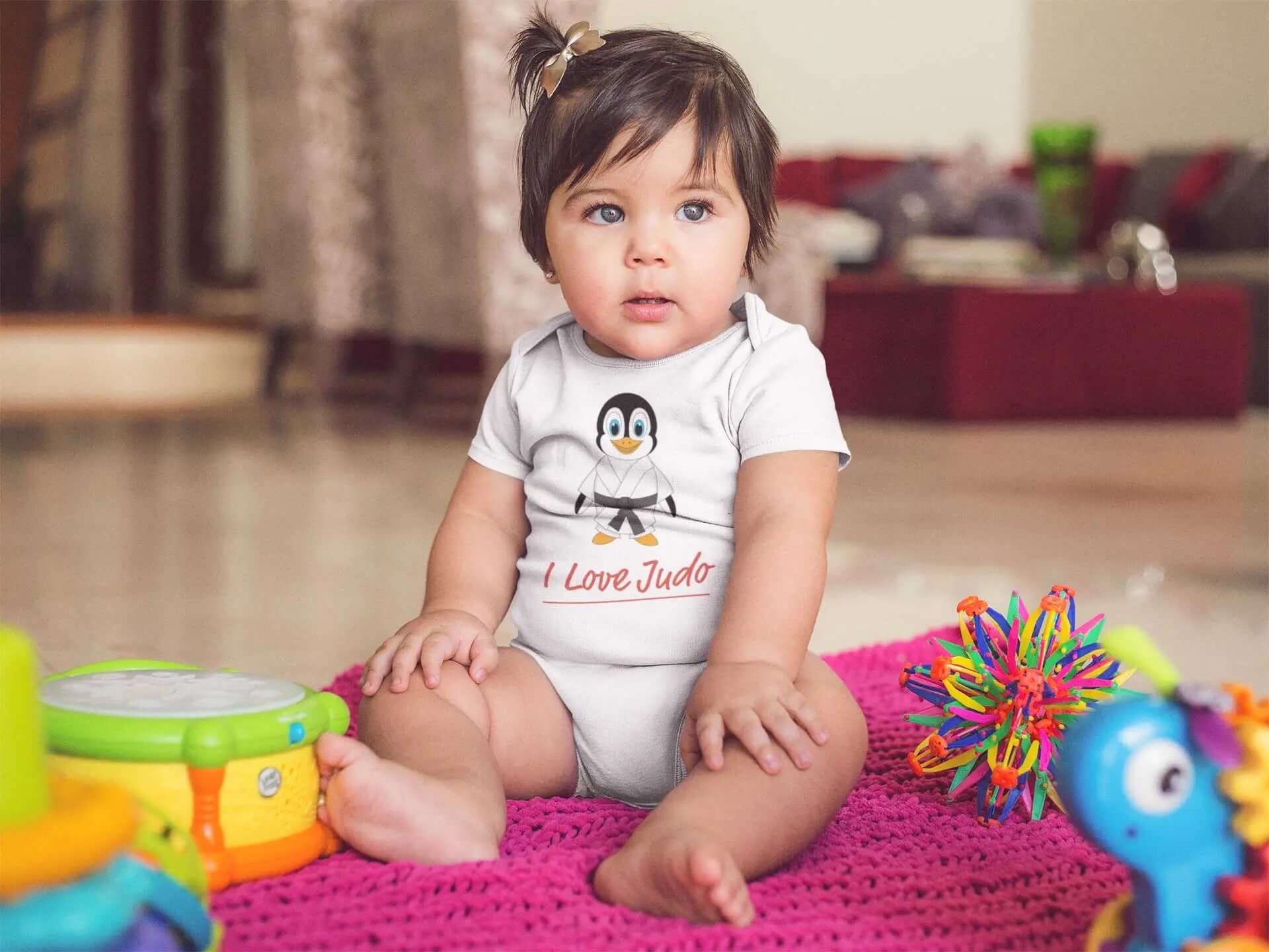Adorable baby wearing a white Judo-themed bodysuit featuring a penguin graphic and 'I Love Judo' text. Perfect for baby and toddler fashion.