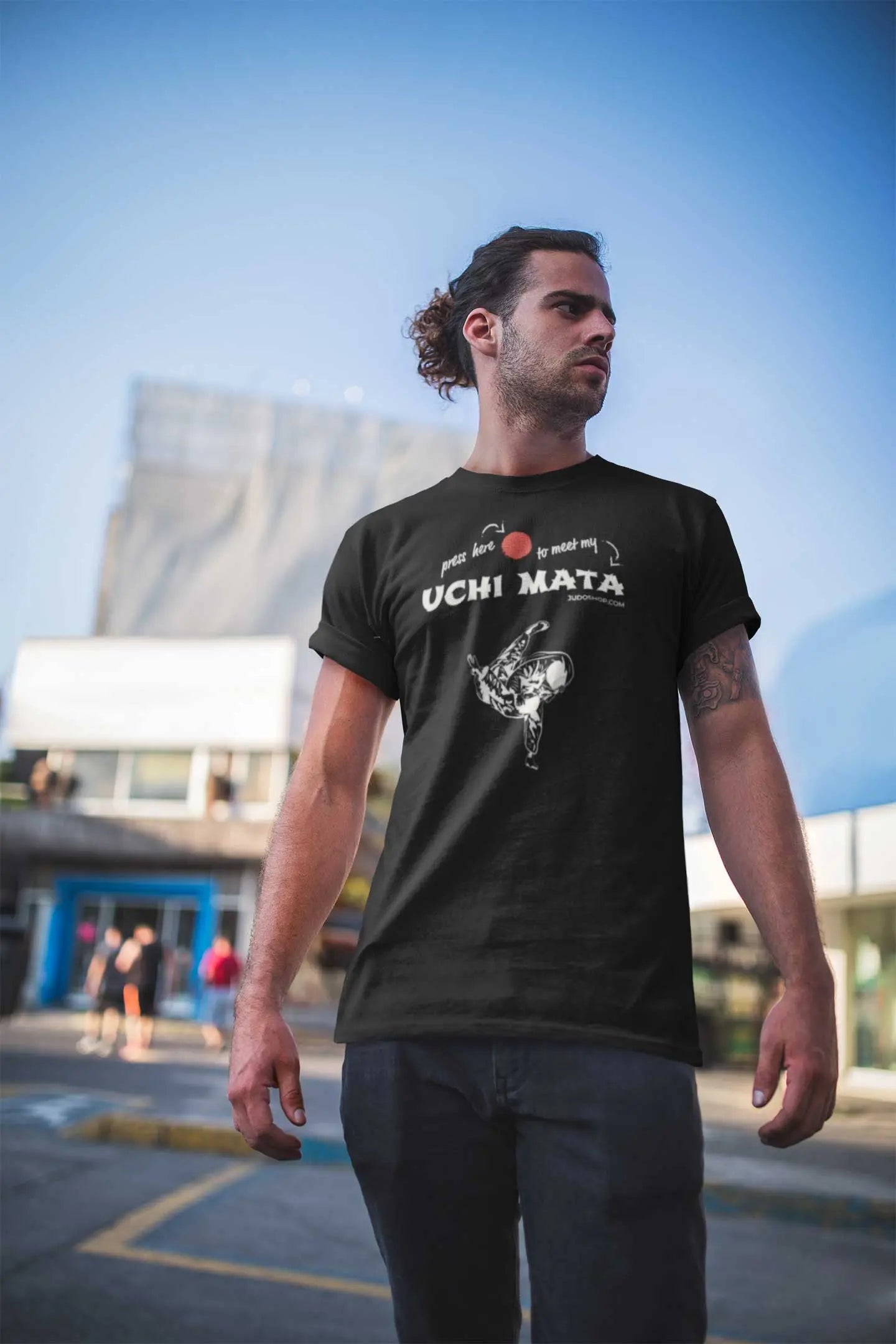 Man standing in an urban setting wearing a black Judo T-Shirt with 'Press here to meet my Uchi Mata' design, perfect for casual outings.