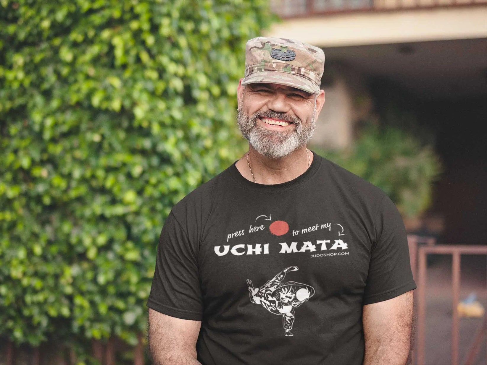 Man in a camouflage hat wearing a black Judo T-Shirt with 'Press here to meet my Uchi Mata' design, casual and sporty.